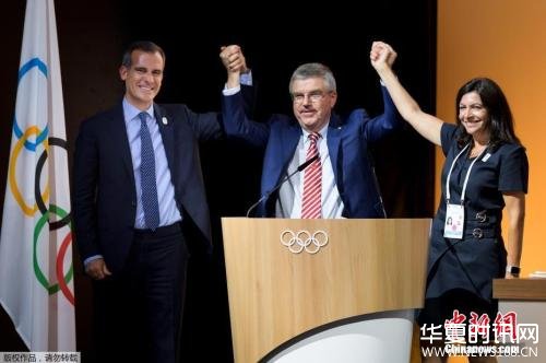 图为投票结束后，洛杉矶市长加塞蒂和巴黎市长伊达尔戈登上主席台，国际奥委会主席巴赫站在中间高举起两人的手表示庆祝。