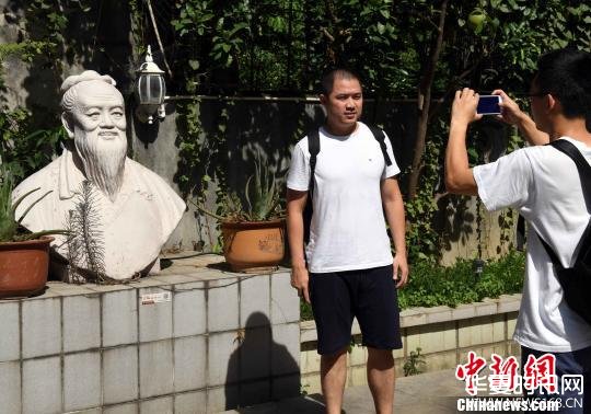 一名男青年在陈一帆雕塑艺术馆前与陈一帆创作的孔子塑像合影。　记者刘可耕 摄